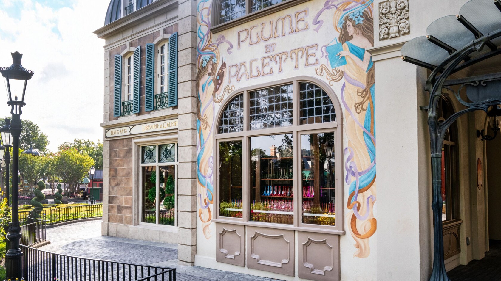 The exterior of Plume Et Palette in Epcot featuring a decorative mural with female figures reading, painting and the stylized name of the store on top