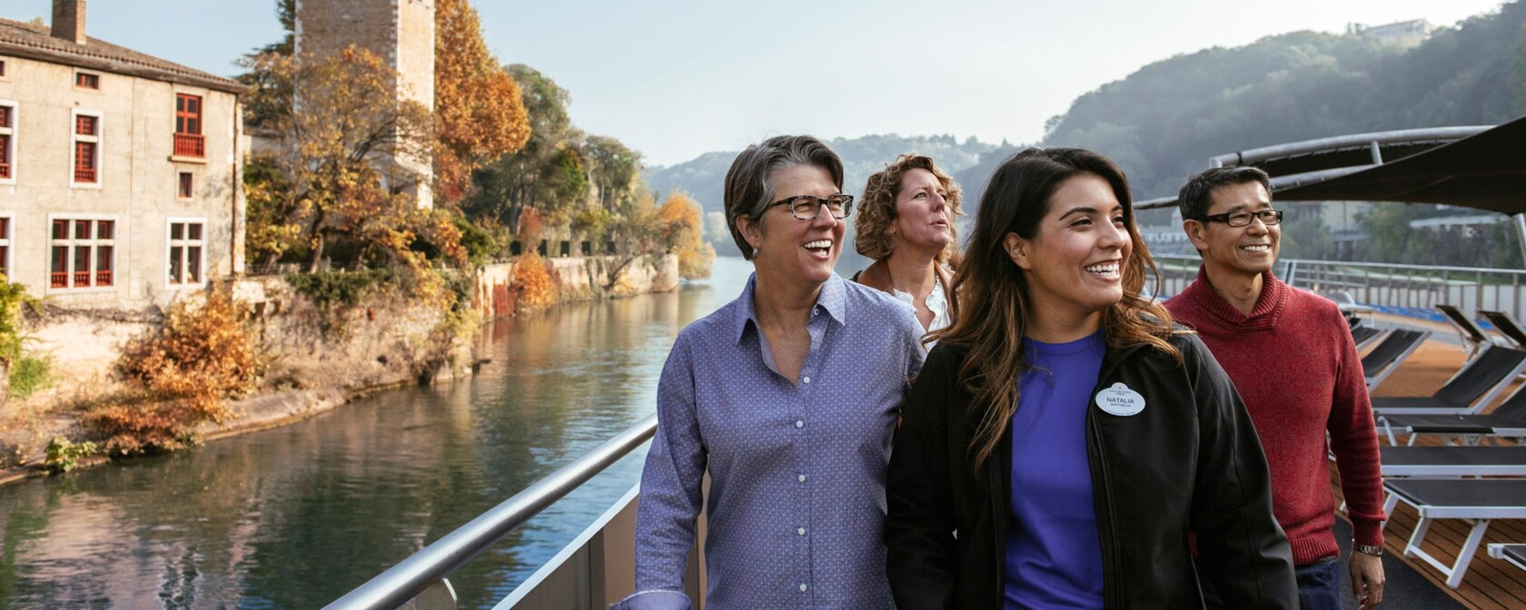 An Adventures by Disney Guide and 3 adult Guests on the deck of a small ship sailing along a river