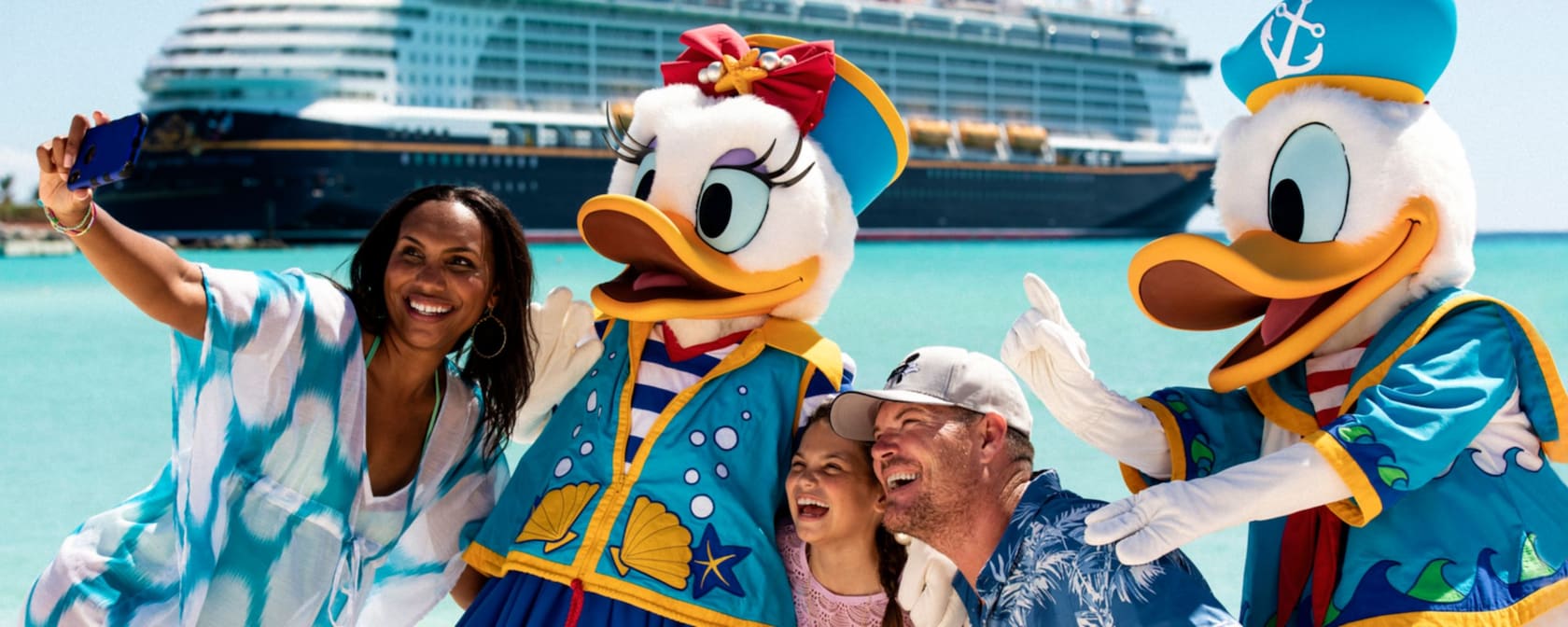 A group of 3 people taking a selfie with Donald Duck and Daisy Duck next to a harbor