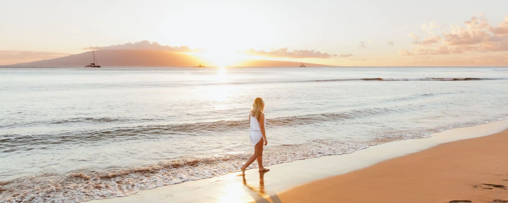 As gentle waves come ashore, a woman walks along the beach at sunset, at the Hyatt Regency Maui Resort and Spa