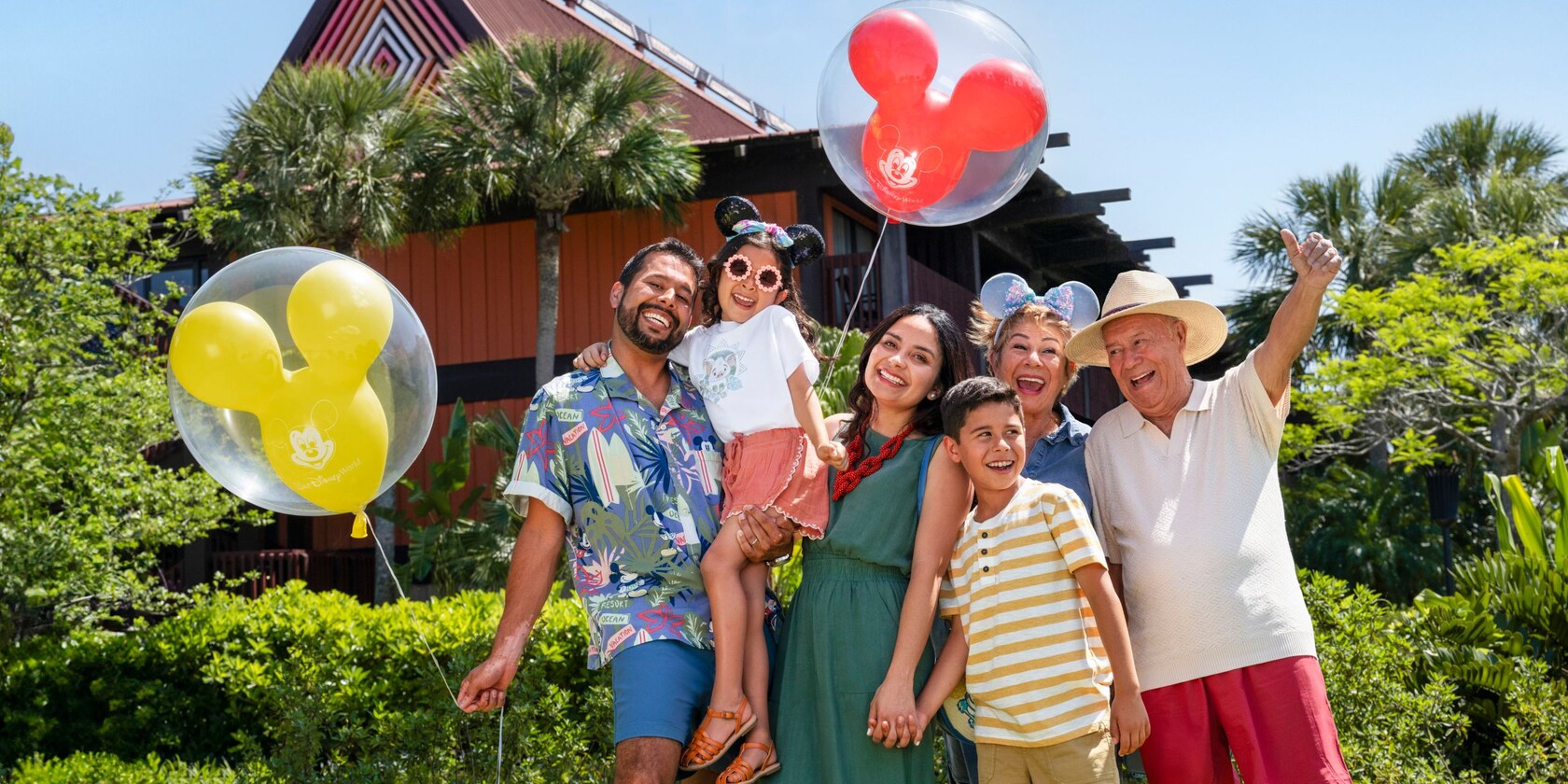 A multi generational family holding Mickey Mouse balloons near Disney's Polynesian Village Resort	
