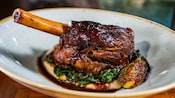 A lamb shank served atop sautéed spinach and parsnip puree