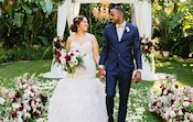 Un couple se tenant la main marche le long d’une allée couverte de pétales de fleurs à l'extérieur.