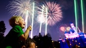 A little boy laughs at fireworks bursting in the sky above Sleeping Beauty Castle
