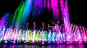 色彩缤纷的灯光闪烁在天堂码头（Paradise Pier）和米奇欢乐摩天轮（ Mickey’s Fun Wheel）附近的喷泉上