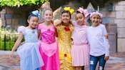 5 名小女孩在睡美人城堡（Sleeping Beauty Castle）外摆好了姿势，她们身着公主服装和配饰，双臂相拥。