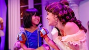 A little girl dressed as a princess smiles with Belle
