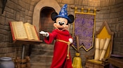 Mickey Mouse dressed as a wizard next to a brook, a book and scrolls
