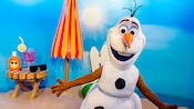 Olaf on a beach next to an umbrella and beach amenities
