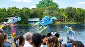 ディズニーキャラクターをイメージに模られた凧のショーを観るためディズニー・アニマルキングダムのラグーン周辺に集まるゲストたちを描いたアーティストコンセプト