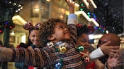 クリスマスイルミネーションを身に着けた子供が雪の結晶に手を伸ばして笑顔を見せる