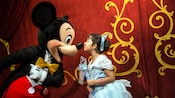 A little girl dressed as a princess kisses Mickey Mouse
