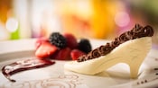 A plate with a white chocolate dessert shaped like a high heel shoe near strawberries