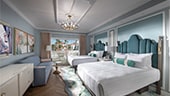 Two queen beds next in a room with balcony doors opposite a flat-panel TV on a wood console