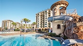 Pool with water slide and palm trees in front of multi story hotel buildings at Disney’s Polynesian Village Resort