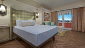 A hotel bedroom with a bed, side table, coffee table, couch and a deck with a boardwalk view