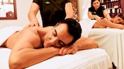 A man and a woman lie on massage tables, getting massages