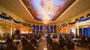 Be Our Guest Restaurant 내부의 테이블과 의자 및 천장의 샹들리에와 천사 문양 모자이크