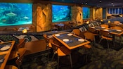 The inside of Coral Reef Restaurant with set tables, chairs and a glass tank filled with sharks and fish