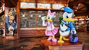 Statues of Donald Duck and Daisy Duck in a store with a sign saying Welcome Pin Traders
