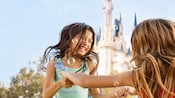 Two little girls play with bubbles in front of Cinderella Castle