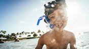 Un niño sonriente en aguas de mar poco profundas, con una máscara de buceo sobre la frente 