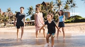 A family of 4 looks toward the ocean as they walk in the shallow water on the beach at Aulani Resort A family of 4 looks toward the ocean as they walk in the shallow water on the beach at Aulani Resort
