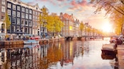 A serene canal in Amsterdam at sunset featuring a walking bridge, ornate buildings and pedestrians eating at a café A serene canal in Amsterdam at sunset featuring a walking bridge, ornate buildings and pedestrians eating at a café