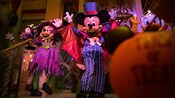 Mickey Mouse in top hat and tails standing next to Minnie Mouse dressed as a not so scary witch
