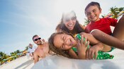 A small girl in an inflatable raft smiles as her family surrounds her at the beach