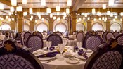 An abundance of cylindrical light fixtures hang from the ceiling over elegant, Rococo style table settings