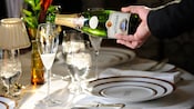 The hand of a sommelier pouring sparkling wine into champagne flutes