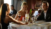 2 women and a man smiling as they sip wine together in a fine dining restaurant