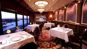 The interior of a fine dining restaurant features linen table cloths, china and large window views of the ocean