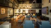 A loft style recreation room with a mix of modular seating, tables, wall art and 2 jumbo screen TVs