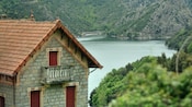 A stone building situated at the edge of a body of water surrounded by a verdant mountain landscape