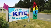 A large, roadside sign identifying the World Kite Museum next to a banner that says Open