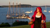 Con un abrigo a la antigua, un artista lleva una canasta y un farol por Bar Harbor, Maine