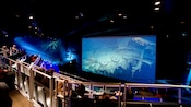 Visitantes en un auditorio mirando una película que muestra el Titanic hundido en el fondo del océano