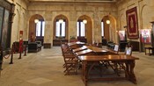 The interior of a stone building reveals high ceilings, an arched promenade and antique desks