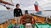 A man looking out to sea while standing at the helm of a sailing boat