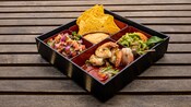 A bento box with shrimp, guacamole, salsa and corn chips