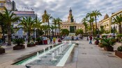 A city square lined with trees, fountains and historic architecture