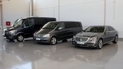 A large luxury van, a midsize luxury van and a luxury sedan, parked indoor