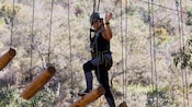Una mujer en una tirolesa caminando sobre troncos suspendidos en la mitad del aire