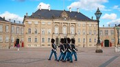 Guards in bearskin hats marching in front of a royal palace