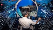 The captain steering the submarine towards an old ship at the bottom of the sea