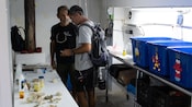 2 men in a lab setting with coral specimens and tubs of water