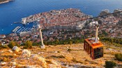 A cable car traveling up a steep mountain near a medieval town and coastline