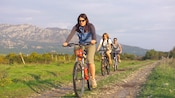 3 bicyclists riding on a dirt path next to pastures and mountains